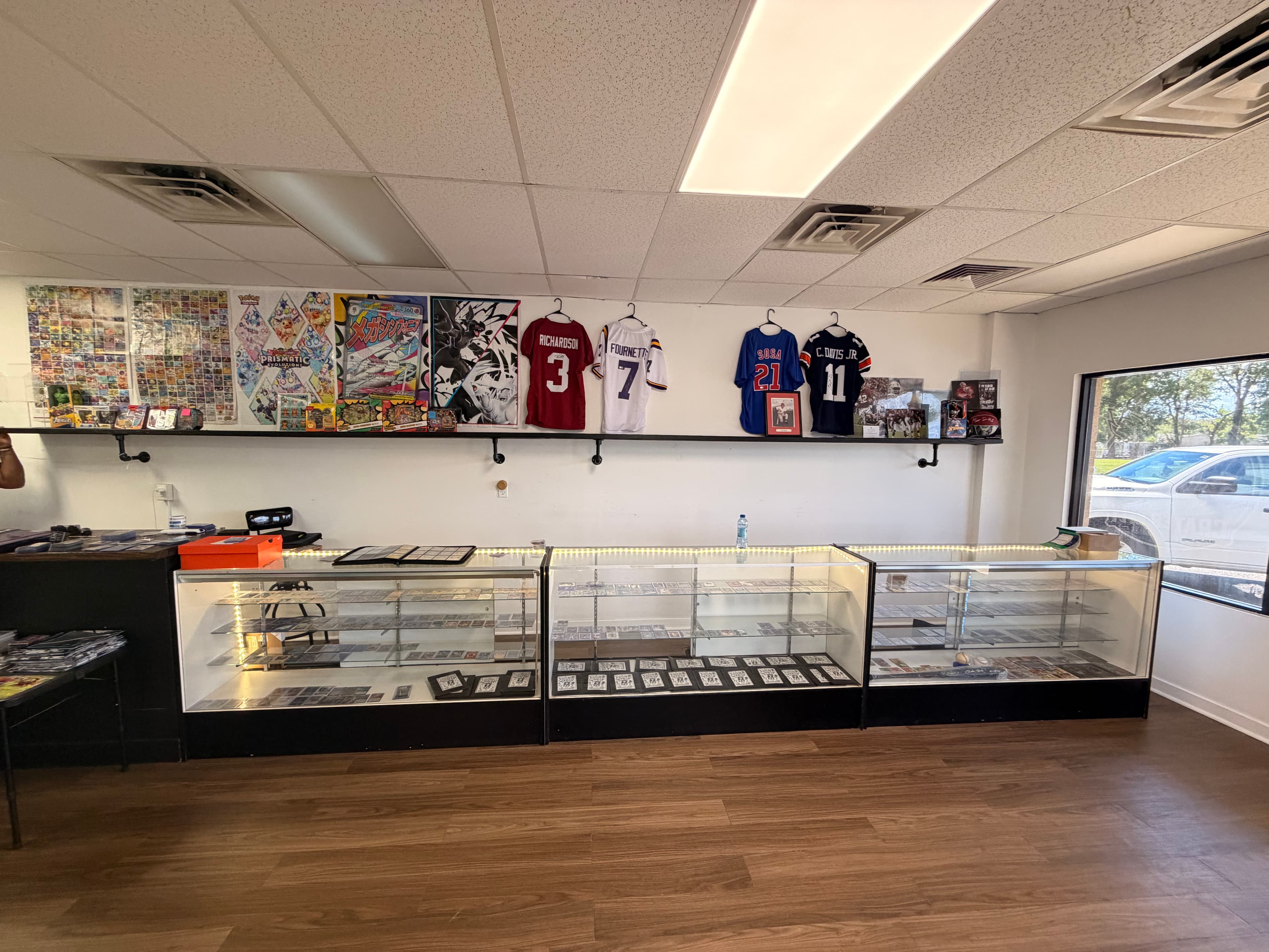 Sports card shop interior with glass display cases, hanging jerseys, and colorful wall posters.